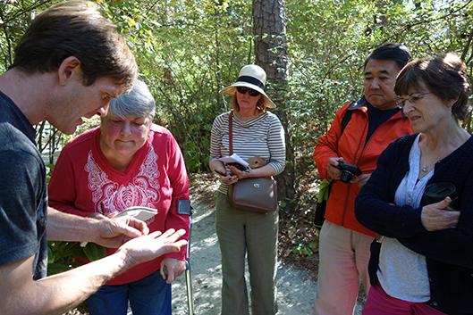 A Gardens tour guide shows a group something in the palm of his hand. A Gardens tour guide shows a group something in the palm of his hand.