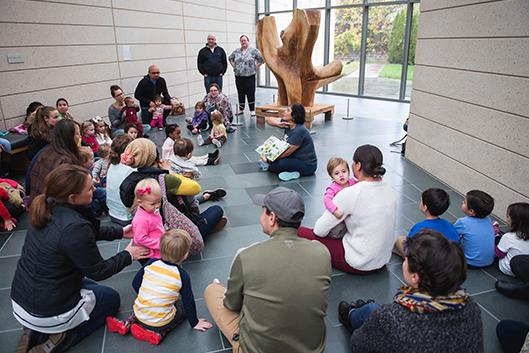 Families with children and babies listen to a story read in Spanish at the Museum