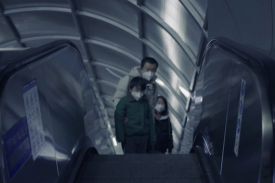 Male adult with two children, all wearing surgical masks, riding up escalator