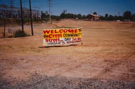 A lone sign stands in an empty land. &quot;Welcome to the Crest Community Street,&quot; it says. A church stands in the background.