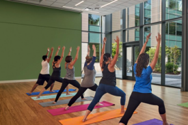 participants standing on colorful yoga mats, arms up towards the ceilings, legs positioned in a forward lunge