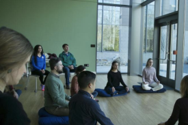 Participants sitting with their legs crossed on meditation pillows, eyes closed, hands placed on their laps.