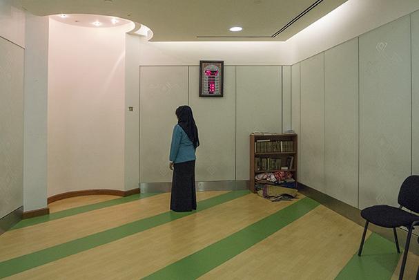 A woman facing Mecca praying in an airport sacred space.