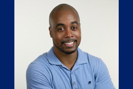Seminar speaker, Dr. Eric Britt Moore, smiling, wearing a light blue collared shirt, and standing in front of a white background