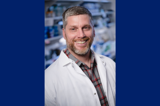 Seminar speaker, Dr. Jason Cannon, wearing a white lab coat while standing in his lab