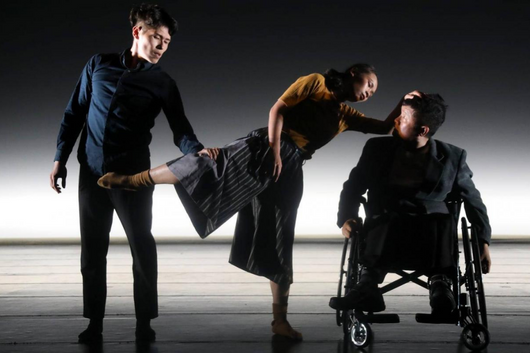 2 standing dancers and one dancer in a wheelchair on stage.