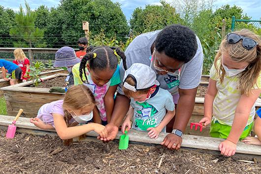 Children gathered around a raised bed planting seeds with the help of an adult