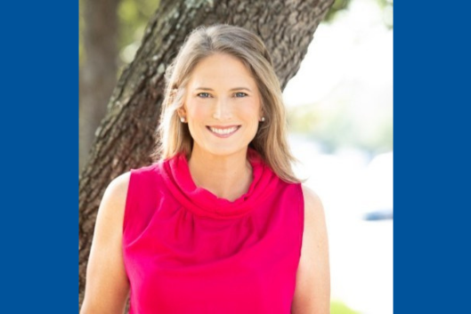 Seminar speaker, Elena Craft, smiling, wearing a pink blouse, with a tree in the background