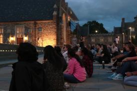 Image of students sitting outside of the Bryan Center Plaza waiting to hear student speakers; Candles placed on the stairs