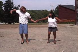 A woman showing a man how to dance outside.