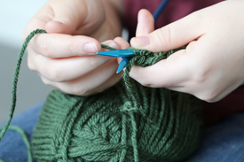 Hands holding knitting needles wrapped in green yarn Hands holding knitting needles wrapped in green yarn