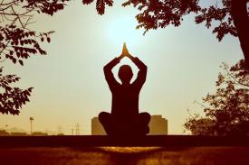 Person meditating, sitting with legs crossed, palms together and raised above head outside in nature Person meditating, sitting with legs crossed, palms together and raised above head outside in nature
