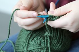 Two hands holding blue knitting needles intertwined in green yarn Two hands holding blue knitting needles intertwined in green yarn