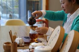 Person pouring tea into a tea cup with a full tea display in front of her Person pouring tea into a tea cup with a full tea display in front of her
