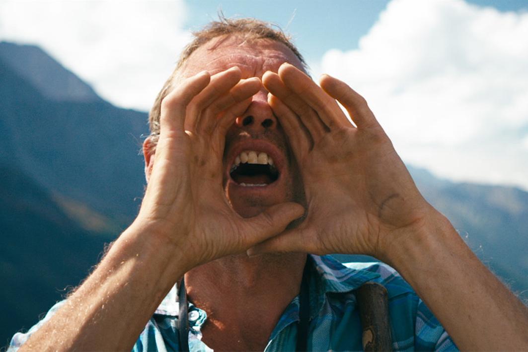 Still from Riafn. A man cups his hands around his mouth and bellows into the distance. Behind him stand the Alps. Still from Riafn. A man cups his hands around his mouth and bellows into the distance. Behind him stand the Alps.
