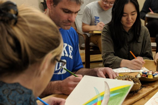 Participants holding color pencils and drawing on white paper.