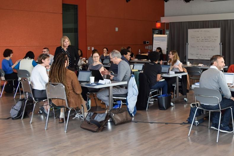 Faculty seated at tables writing on laptops and talking Faculty seated at tables writing on laptops and talking