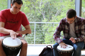 Participants sitting in chairs with drums in between their legs, using their palms to make sound on the drum. Participants sitting in chairs with drums in between their legs, using their palms to make sound on the drum.