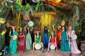 As Karuana, a group of 9 women dressed in colorful dresses with drums and other musical instruments