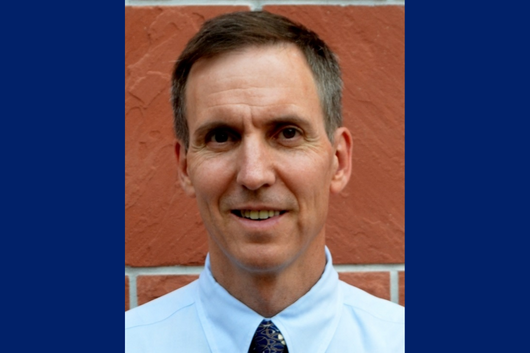 Headshot of seminar speaker, Dr. Jeff Burgess, wearing a collared shirt and tie, standing in front of a red brick wall