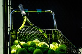 A tennis racket rests in a ball hopper.