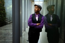 Gregory Tardy standing against a glass wall with his reflection mirrored in it.