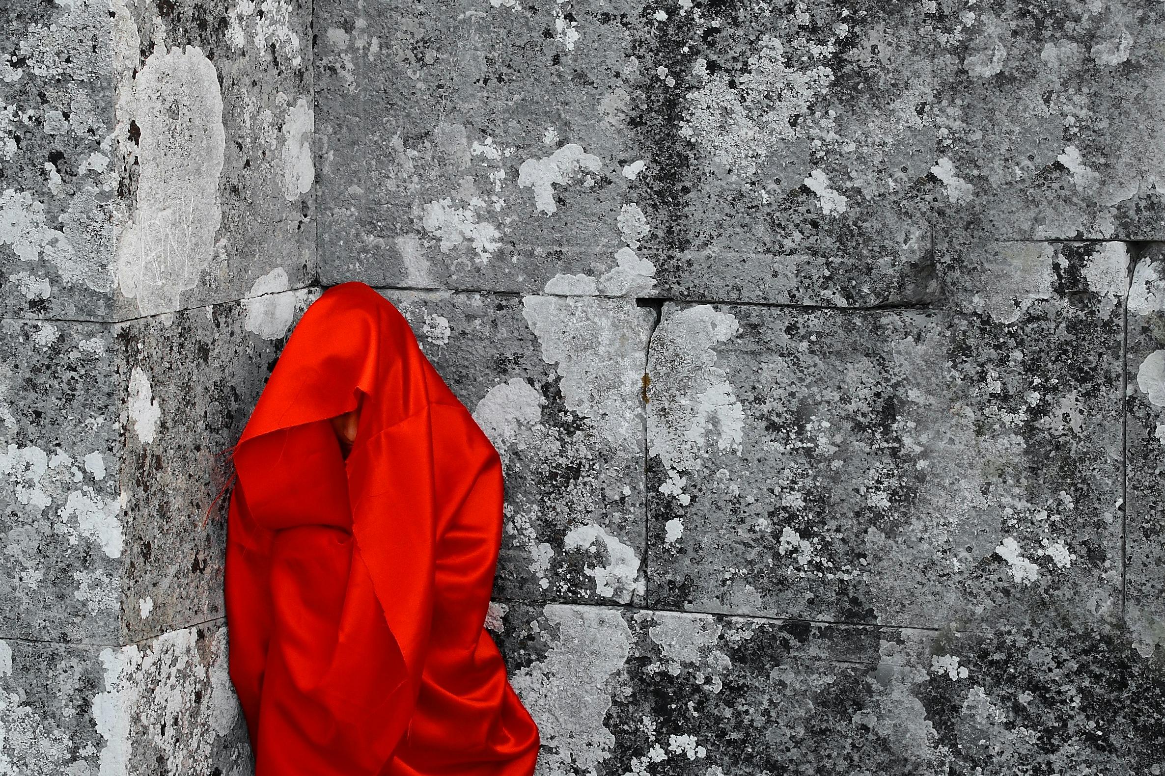 Figure in red silk standing against stone wall