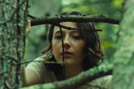 A girl with shoulder length brown hair peers through the branches of a tree in a still from the film Good One.