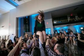 student is lifted in the air while sitting in a chair, crowd around her cheers