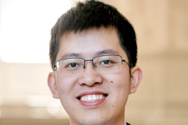 Researcher with dark hair and glasses stands in a blue suit with a maroon striped tie