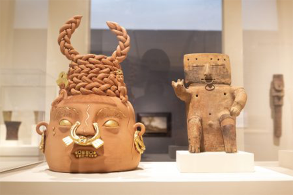 Gallery pairing of a contemporary ceramic work, Pobre Diabla (2022) by artist Joel Gaitan, with a 1000-year-old Seated Male Figure made by the Quimbaya people of Colombia—both with gold nose rings. Photo by J Caldwell.