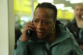 A black woman in a green jacket takes a phone call in a still from Hard Truths